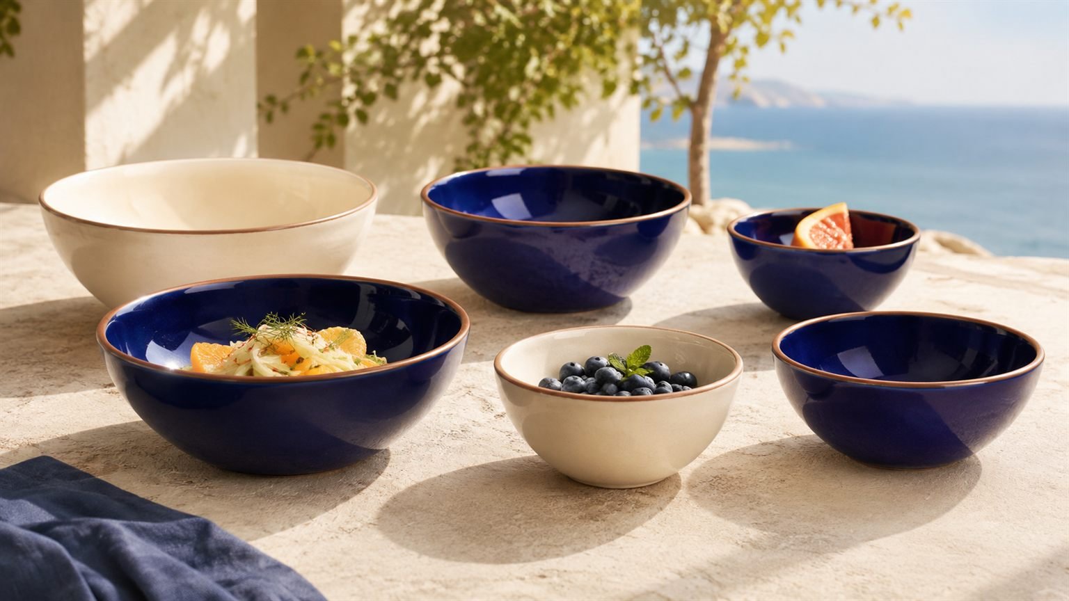 Deep cobalt and cream Verllage stoneware bowls with fruit on a stone terrace overlooking the sea